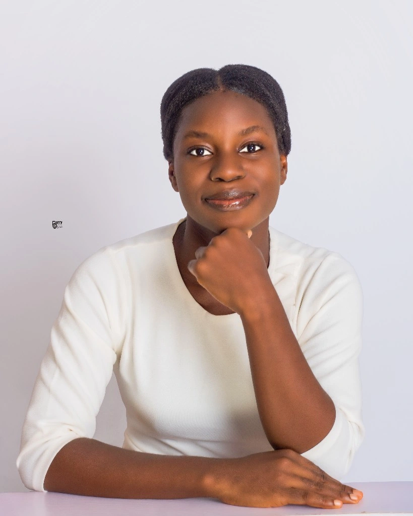 A young woman with a thoughtful expression, resting her chin on her hand, wearing a white long-sleeve shirt, against a light background.