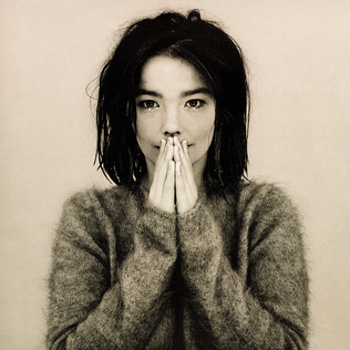 A close-up portrait of a woman with messy hair, wearing a fluffy sweater, and holding her hands together in front of her face, conveying a contemplative or vulnerable expression.