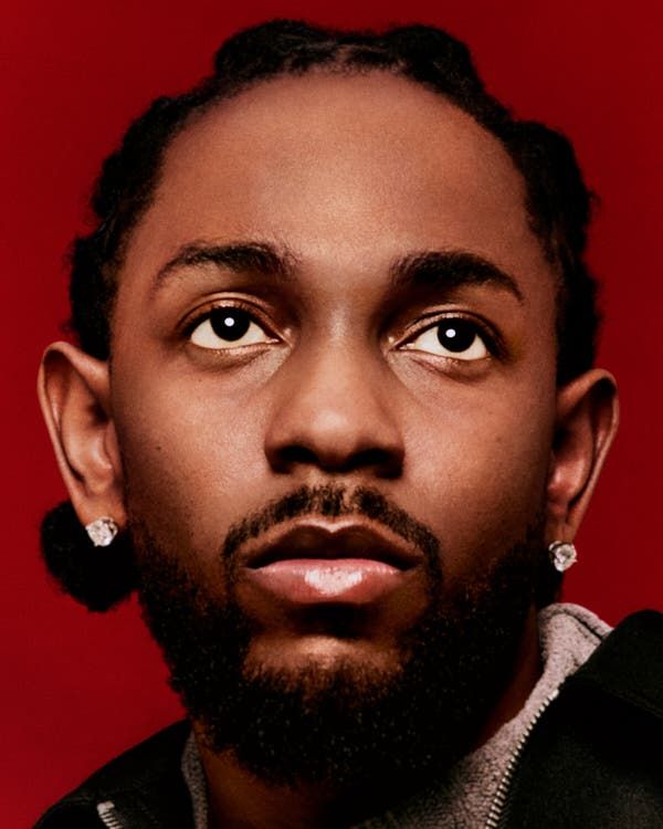A close-up portrait of a man with braided hair and earrings, looking upward against a red background.